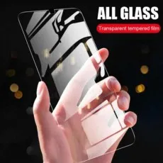 A hand holding an ultra-clear all-glass transparent tempered screen protector, reflecting light and surroundings.