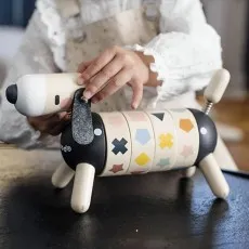a  child’s hands hold a wooden toy dog with a segmented body decorated with colorful shapes.