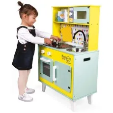 A child stands next to a wooden toy kitchen with a stove, oven, sink, and microwave.