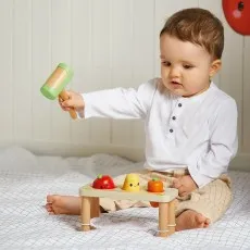 A happy toddler stands in a wooden learning tower with a chalkboard, clapping his hands.