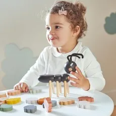 A young child plays with a wooden ant toy and colorful leaf-shaped blocks.