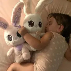 A child sleeping peacefully in bed, cuddling a pink and a white stuffed bunny.