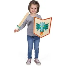 A smiling young girl in jeans and a gray shirt holds a wooden toy sword and a shield with a blue dragon design