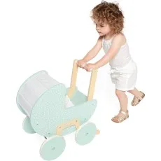 A toddler with curly hair pushing a mint-green Janod wooden toy pram with a white speckled pattern and wooden handle