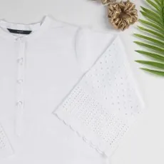 Close-up flat lay of a white eyelet boho blouse with embroidered bell sleeves and button details.